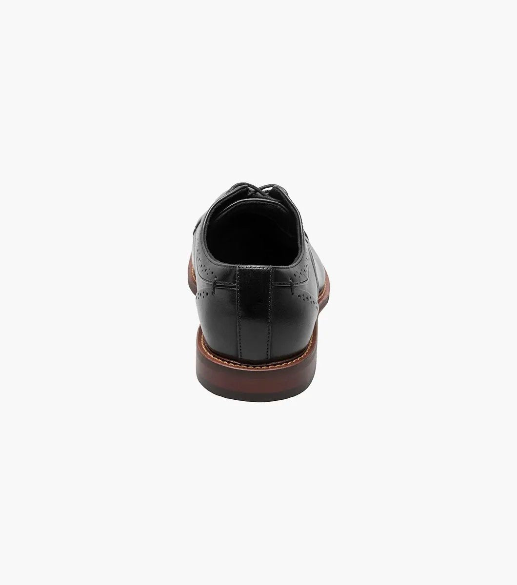 The Stacy Adams - MADDOX Cap Toe Oxford shoe features a black smooth leather finish with a polished appearance, complemented by a brown sole, intricate decorative stitching, and anatomical arch support.