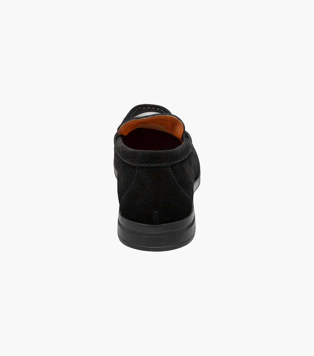 Introducing the Stacy Adams - PALLADIAN Moc Toe Slip On in black suede, featuring a moc toe and metal buckle detail. This stylish shoe includes a cushioned insole, low heel, and visible stitching all presented on a sleek white background.