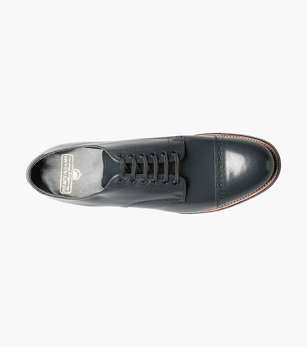 Explore the sophistication of the Stacy Adams MADISON Cap Toe Oxford in navy kidskin leather. This design includes closed lacing, a round toe, and decorative perforations. A cap toe and stacked heel complete the look against a pristine white background.