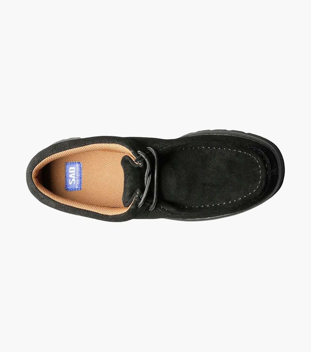 The Stacy Adams DETONATOR Moc Toe Chukka in black suede (63027-11) boasts soft suede material and laces, complemented by its oversized lug sole. Its thick, grooved rubber base enhances both style and comfort against a white background.