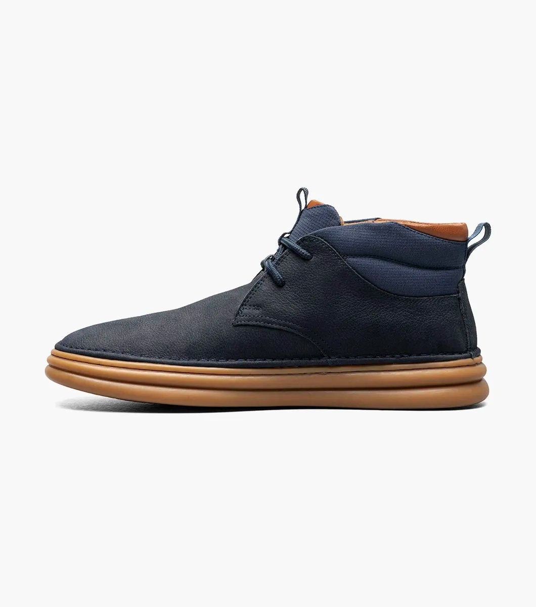 The Stacy Adams DELSON Plain Toe Chukka Boot in Navy showcases a leather upper paired with brown soles and laces, featuring anatomical arch support, set against a white background.