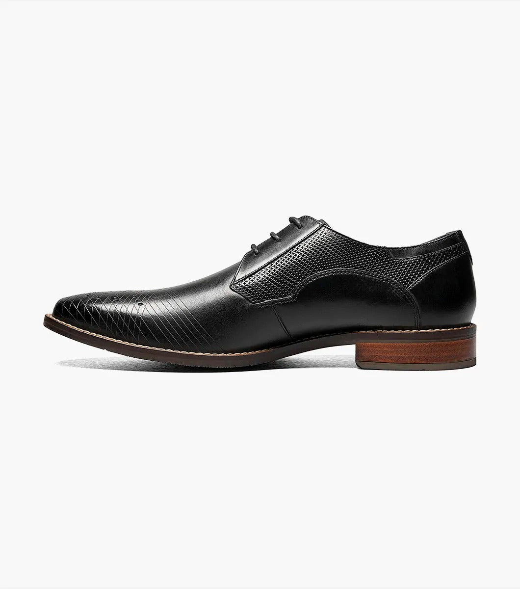 The Stacy Adams - JOVIAN Plain Toe Laser Oxford in black, product code 25504-001, is a premium dress shoe boasting a lace-up closure and distinctive brown detailing on the sole. Made from laser-treated leather for a sleek finish, it includes a Memory Foam insole to enhance comfort.