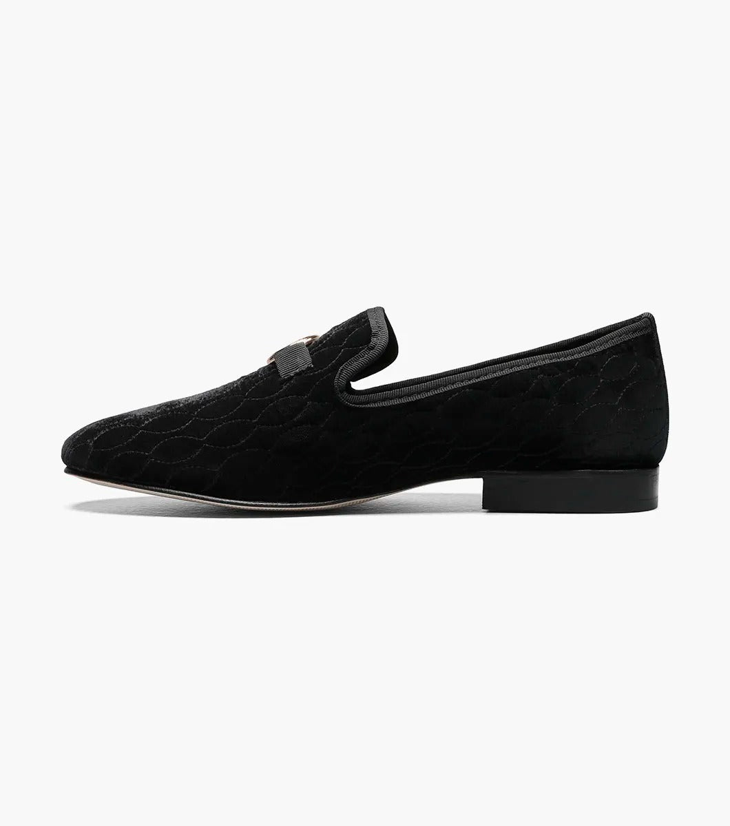 The Stacy Adams VALET Slip On Bit Loafer in Black (25166-001) showcases a black velvet design with a quilted pattern and gold emblem on top, enhanced by a genuine leather sole and cushioned with a Memory Foam insole for superior comfort.