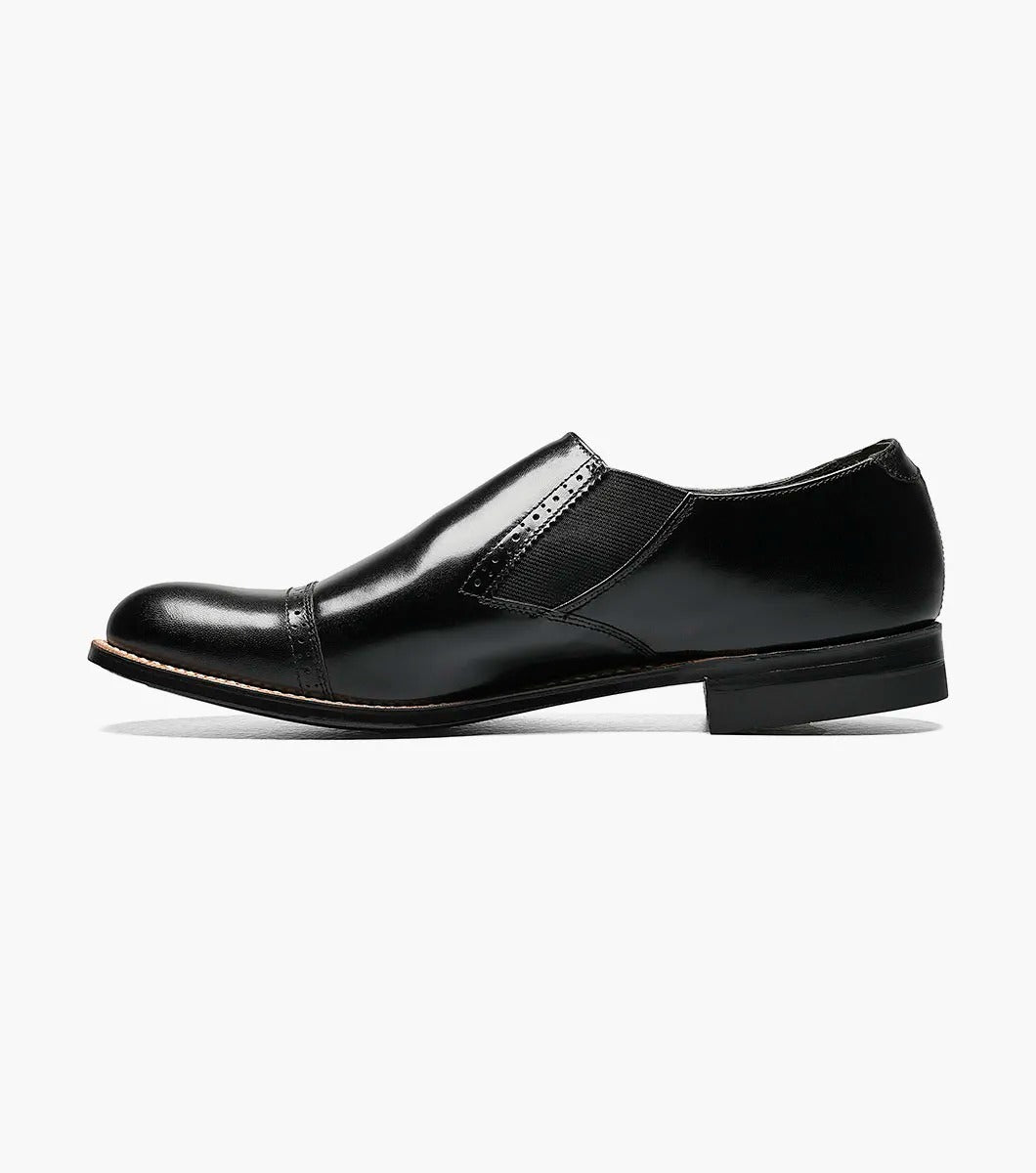 The Stacy Adams MADISON Cap Toe Slip On in black, designated as style number 00017-01, features a sophisticated cap-toe design with elastic side panels, complemented by a leather sole and sleek low heel.