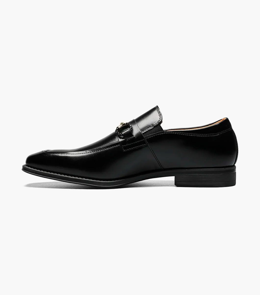 The Stacy Adams PIERCE Moc Toe Bit Slip On in black, style number 25245-001, features a metallic buckle detail and a low heel. It comes with a comfortable Memory Foam insole and is displayed against a white background.