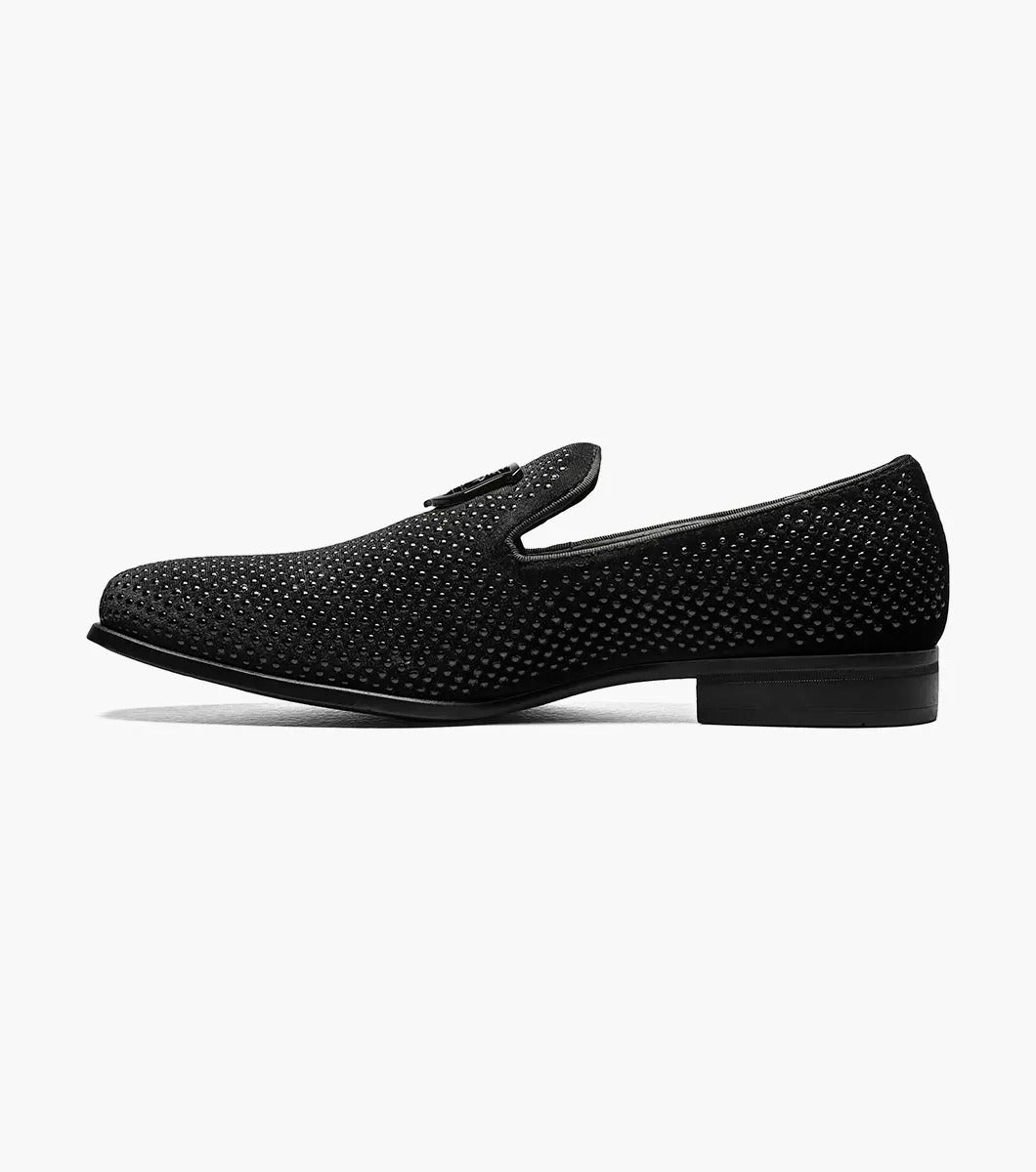 The Stacy Adams - SWAGGER Studded Slip On in black (style 25228-001) features a striking silver emblem, accompanied by a textured design and low heel. These shoes offer a sophisticated touch with the added comfort of memory foam, making them ideal for any occasion.