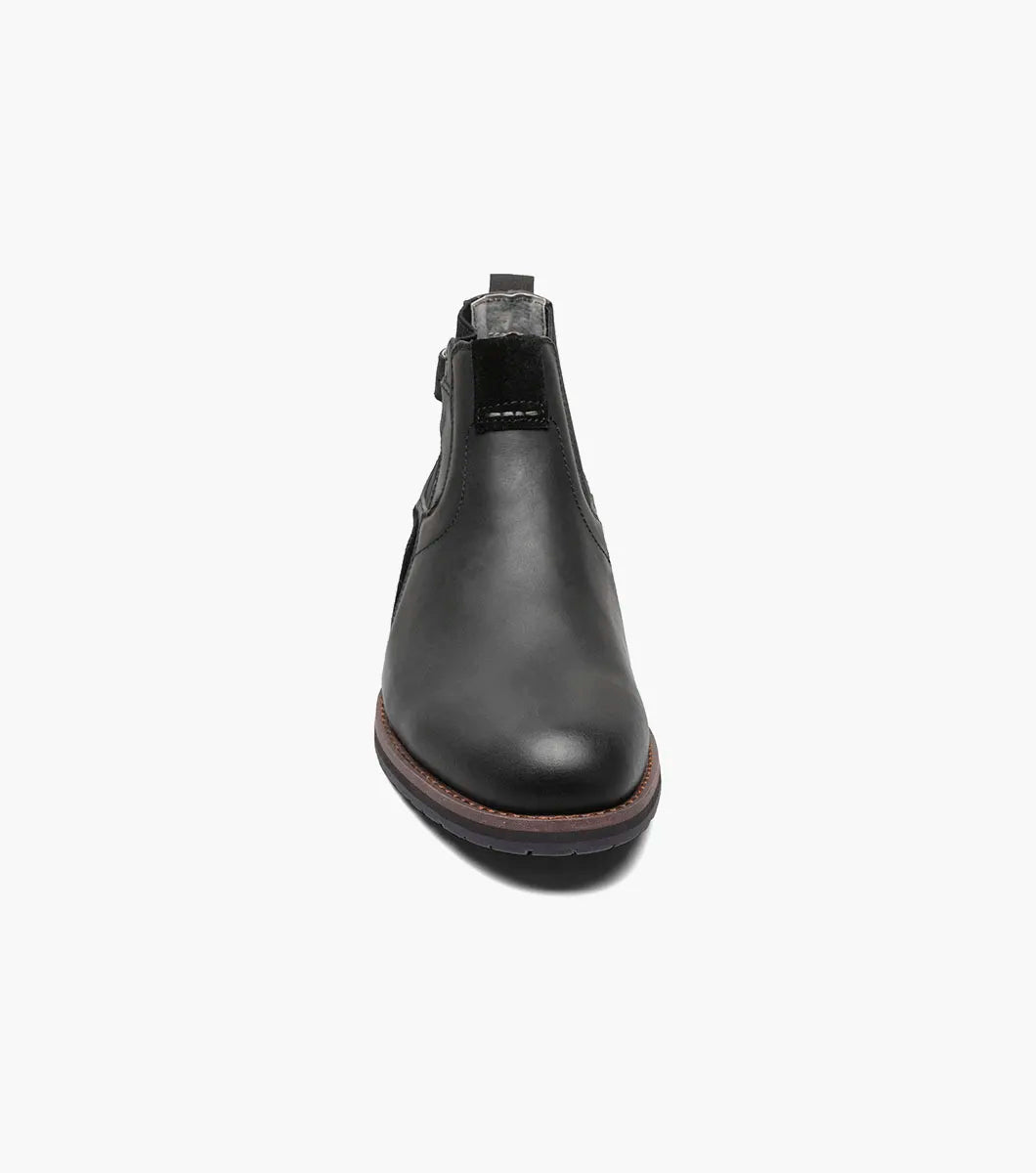 The Stacy Adams OSKAR Plain Toe Chelsea Boot in Black Waxy features a black leather design with a side buckle, an elastic gusset, and a brown sole. Its stylish mixed material upper adds an extra touch of flair.