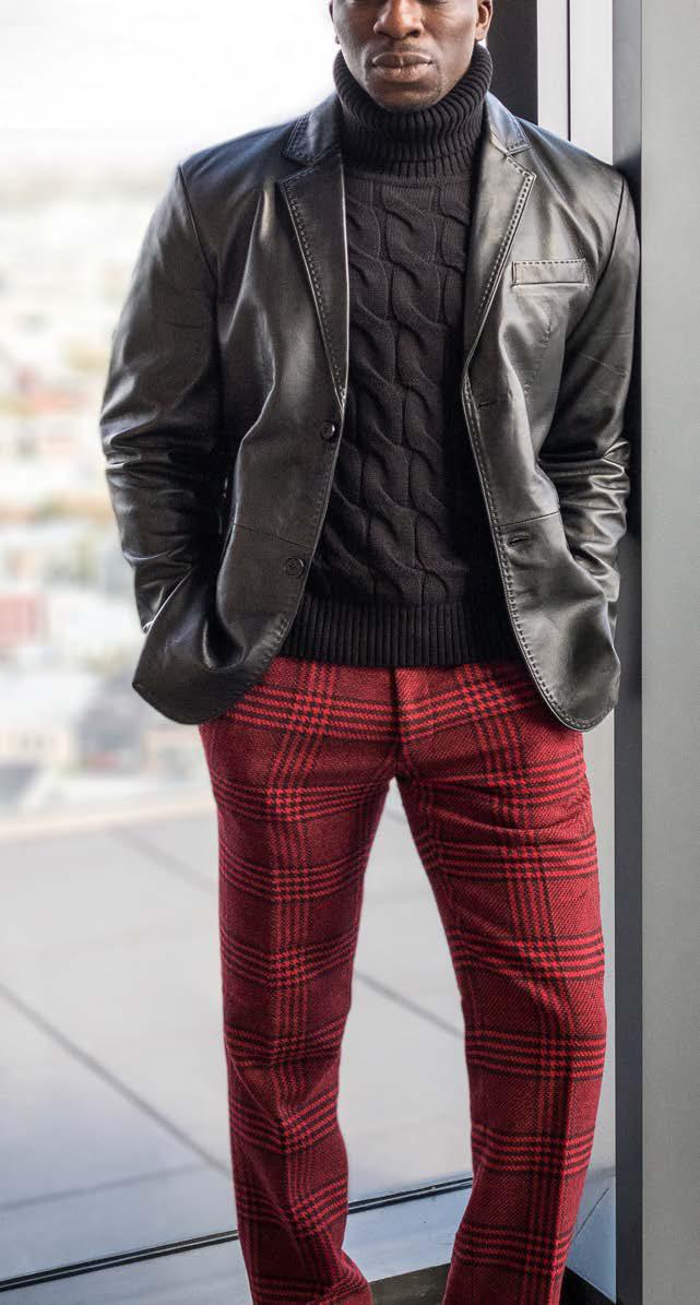 A person wearing the Inserch Lamb Leather Blazer 600-01 in black, featuring subtle pick-stitching, over a black turtleneck sweater and red plaid pants, stands indoors.