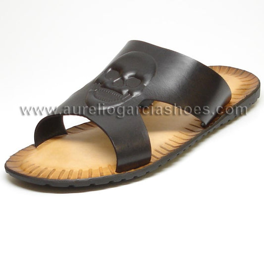 The FI-4048 Black Encore by Fiesso is a stylish black leather sandal featuring a skull design on the strap and a tan sole, complete with visible stitching and a textured edge, perfectly blending style with comfort.