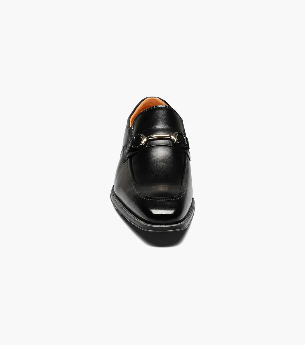 The Stacy Adams PIERCE Moc Toe Bit Slip On in black, style number 25245-001, features a metallic buckle detail and a low heel. It comes with a comfortable Memory Foam insole and is displayed against a white background.