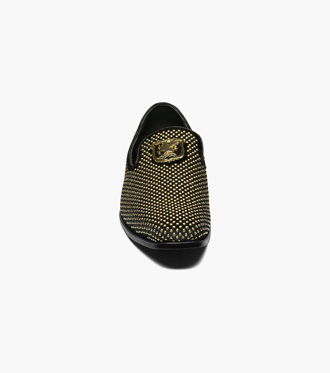 The Stacy Adams - SWAGGER Studded Slip On - Black and Gold - 25228-715 is a black loafer adorned with gold studs and a decorative emblem on top, featuring a comfortable memory foam insole.