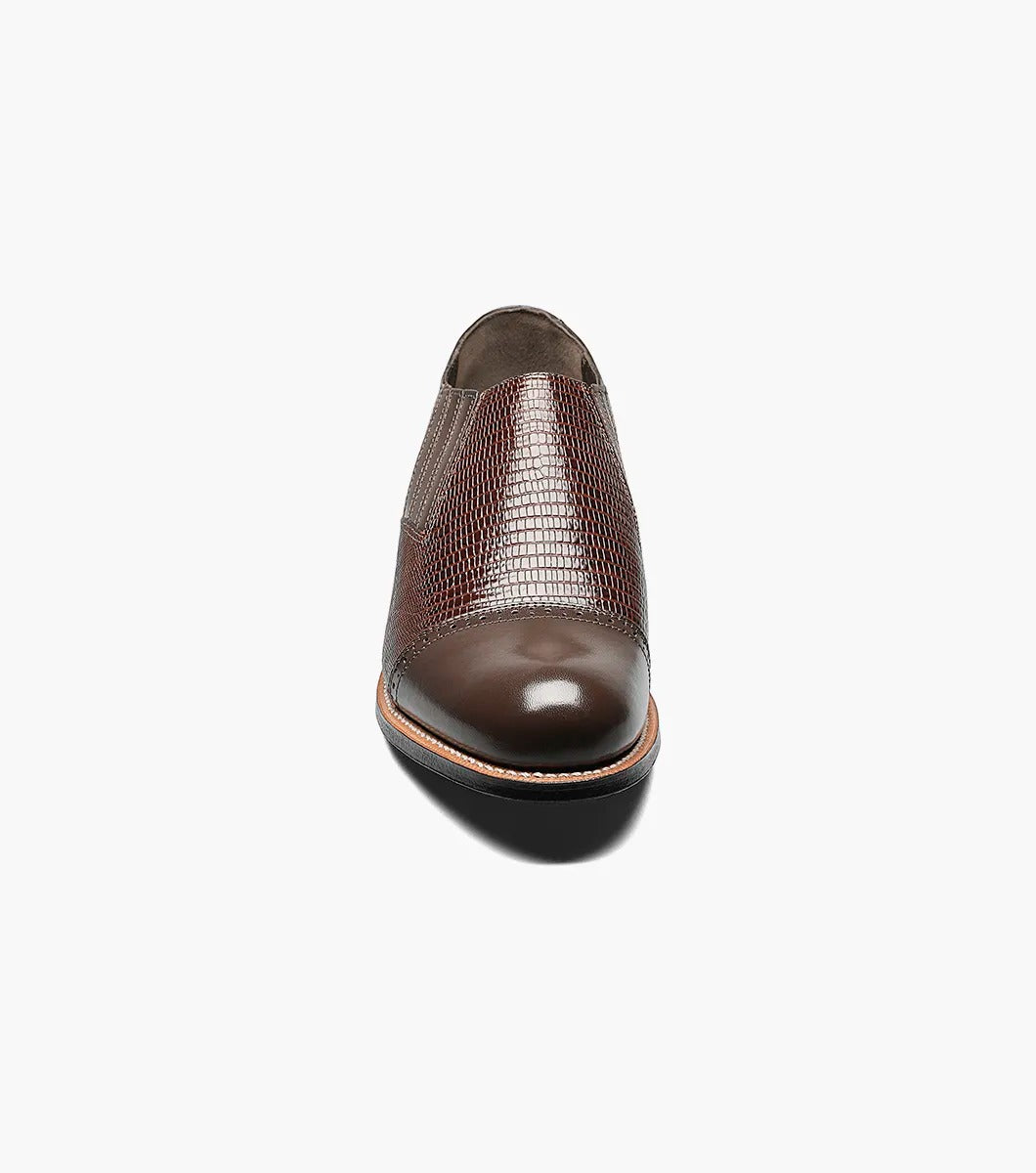 The Stacy Adams - MADISON Cap Toe Slip On in brown is shown in a side profile view against a white background. This shoe features embossed detailing and a low heel, crafted with Goodyear welt construction.