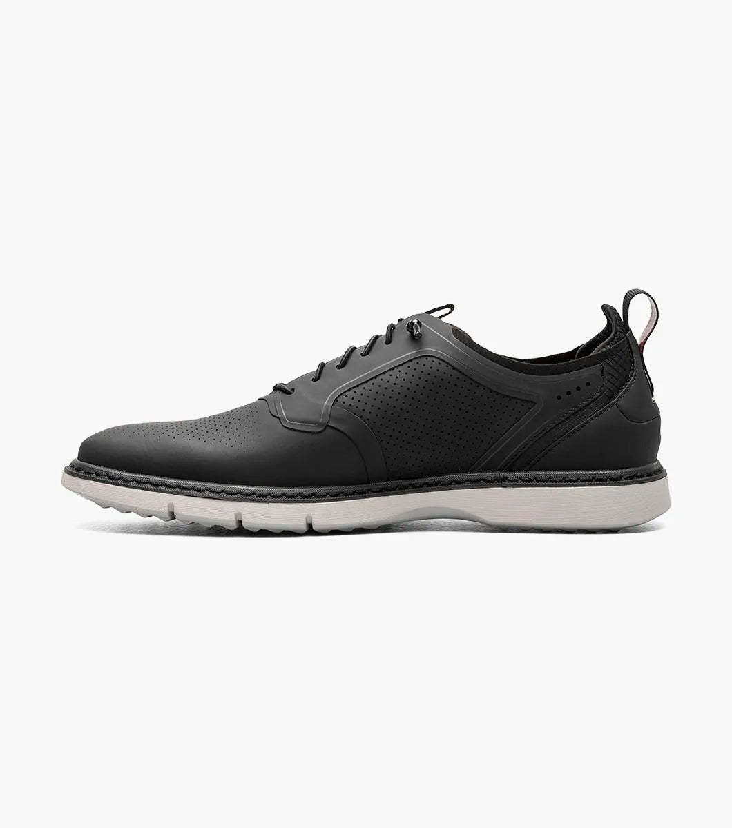 The Stacy Adams SYNCHRO Plain Toe Elastic Lace Up shoe in black (style 25518-001) is a casual dress shoe featuring an elastic lace-up design with a perforated pattern and white sole, complemented by the comfortable RedZone footbed. It is showcased from the side against a simple backdrop.