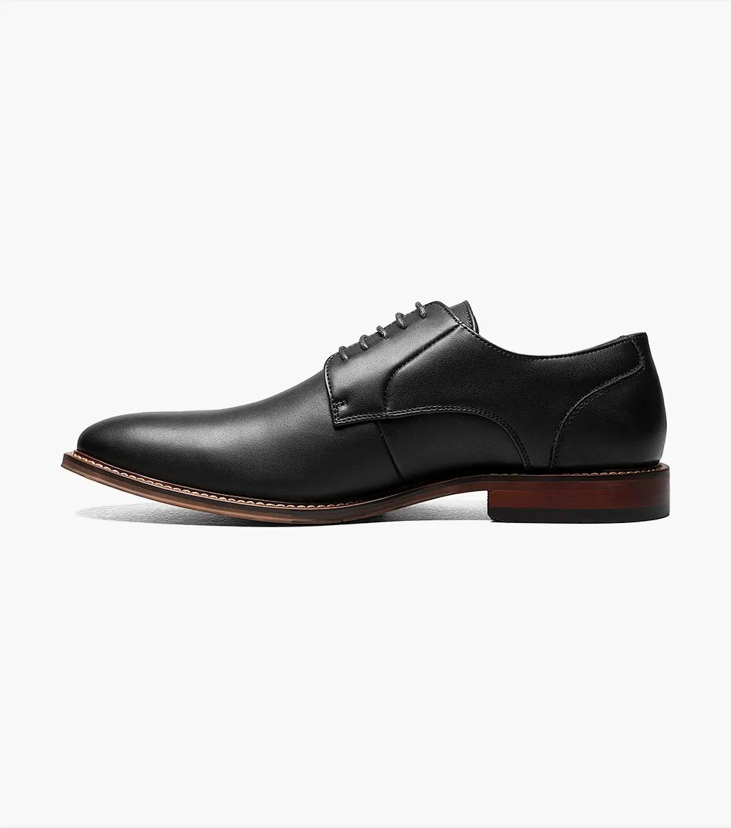 A single Stacy Adams - MARLTON Plain Toe Oxford in black leather, featuring laces, a burnished finish, brown sole, slight heel, and anatomical arch support is displayed on a plain white background.