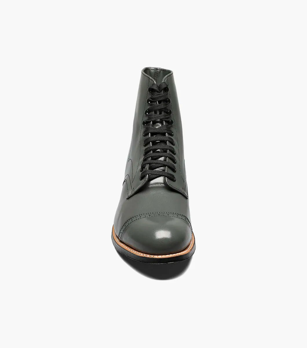 The Stacy Adams MADISON Cap Toe Boot in Steel Gray, made from high-quality kidskin leather, showcases a sophisticated lace-up design and a polished cap toe, enhanced by a sturdy black sole set against a crisp white backdrop.