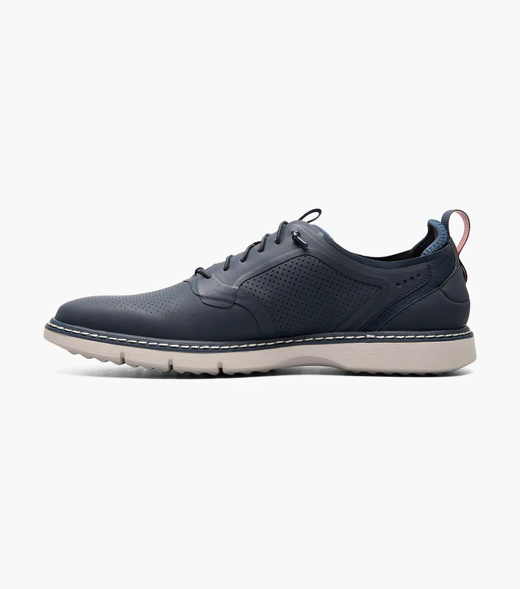 The Stacy Adams SYNCHRO Plain Toe Elastic Lace Up shoe in navy boasts a perforated pattern and a red pull tab, complemented by a light gray sole. It is designed with the RedZone removable footbed to provide anatomical arch support.