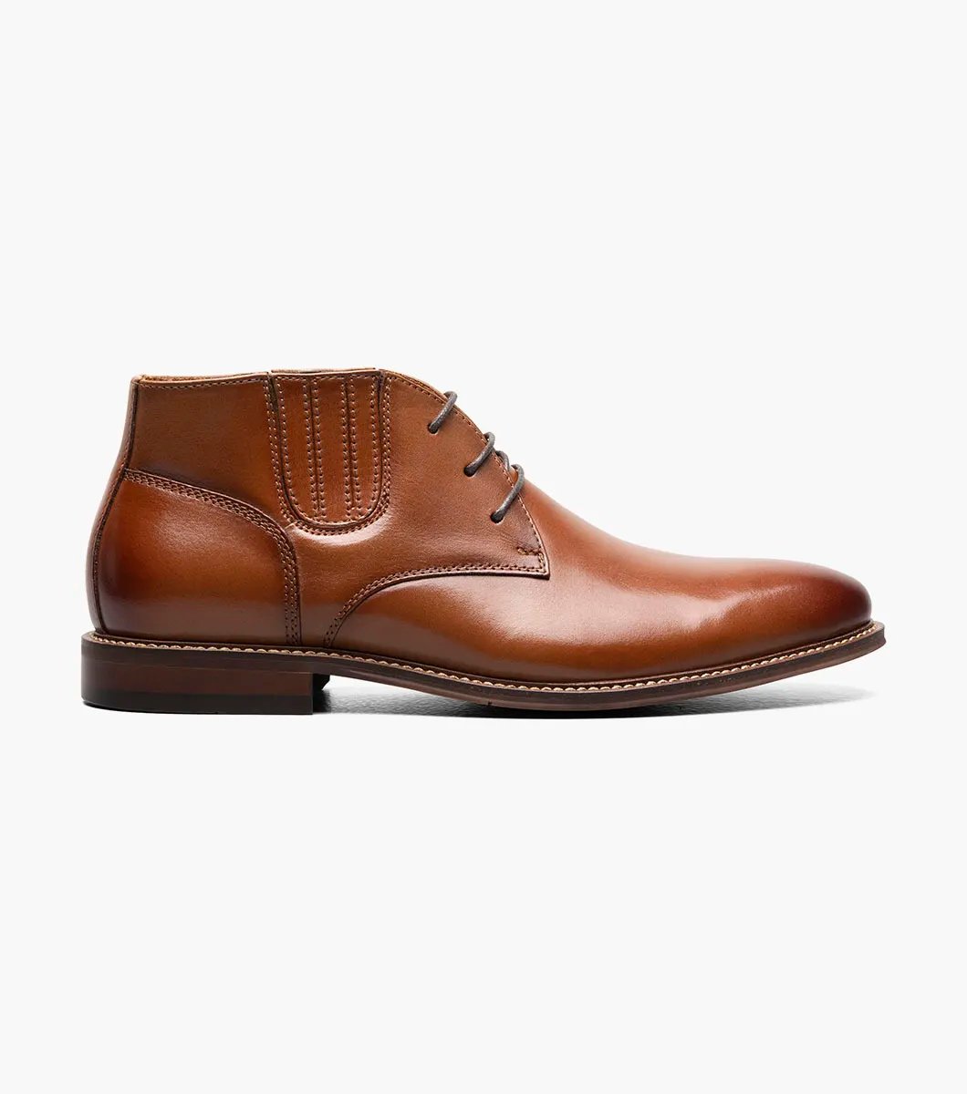 The Stacy Adams Maxwell Plain Toe Chukka Boot in Cognac features a sophisticated leather design with three eyelets, detailed stitching, and a versatile low heel, making it ideal for both dressy and casual events.