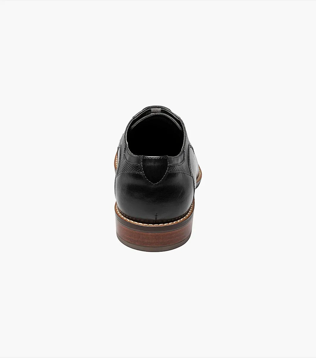 The Stacy Adams - JOVIAN Plain Toe Laser Oxford in black, product code 25504-001, is a premium dress shoe boasting a lace-up closure and distinctive brown detailing on the sole. Made from laser-treated leather for a sleek finish, it includes a Memory Foam insole to enhance comfort.