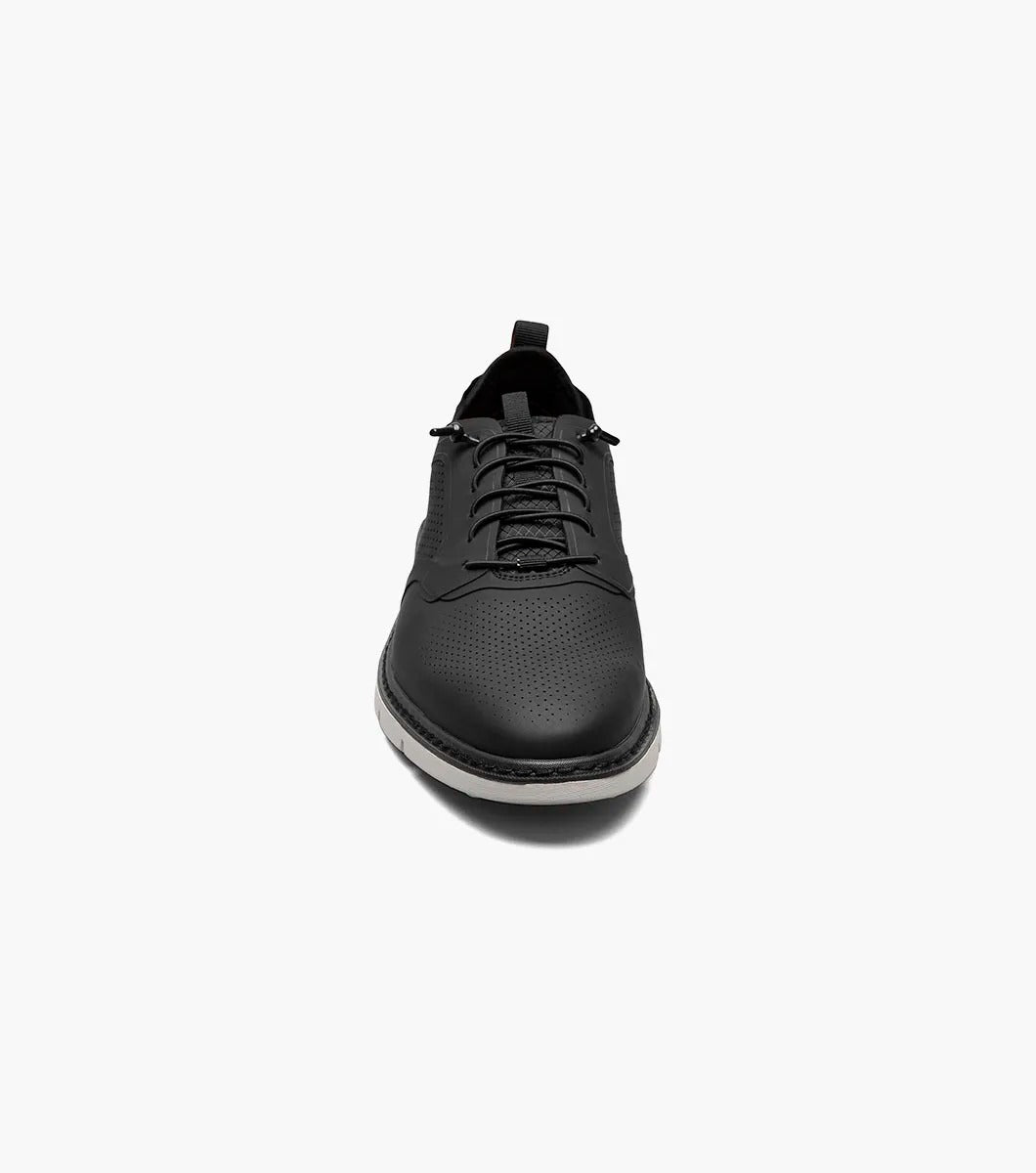 The Stacy Adams SYNCHRO Plain Toe Elastic Lace Up shoe in black (style 25518-001) is a casual dress shoe featuring an elastic lace-up design with a perforated pattern and white sole, complemented by the comfortable RedZone footbed. It is showcased from the side against a simple backdrop.