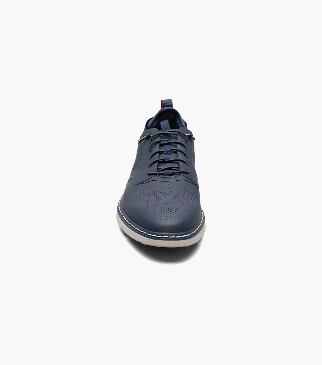 The Stacy Adams SYNCHRO Plain Toe Elastic Lace Up shoe in navy boasts a perforated pattern and a red pull tab, complemented by a light gray sole. It is designed with the RedZone removable footbed to provide anatomical arch support.