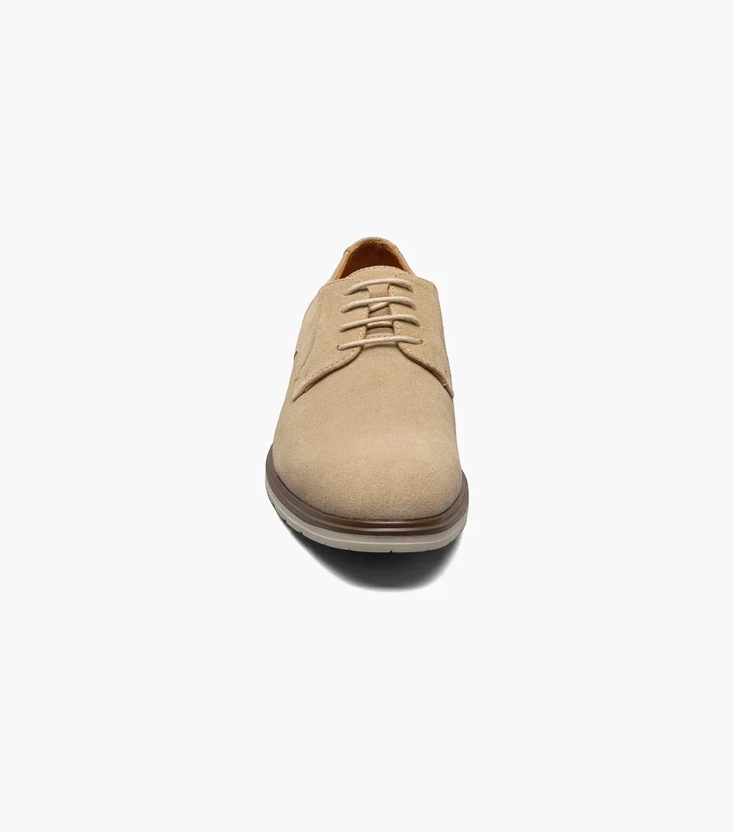 The Stacy Adams TAYSON Plain Toe Lace Up in sandstone is an Oxford shoe made from tan suede. It features anatomical arch support and laces, complemented by a light brown sole. The shoe is displayed against a plain white background.