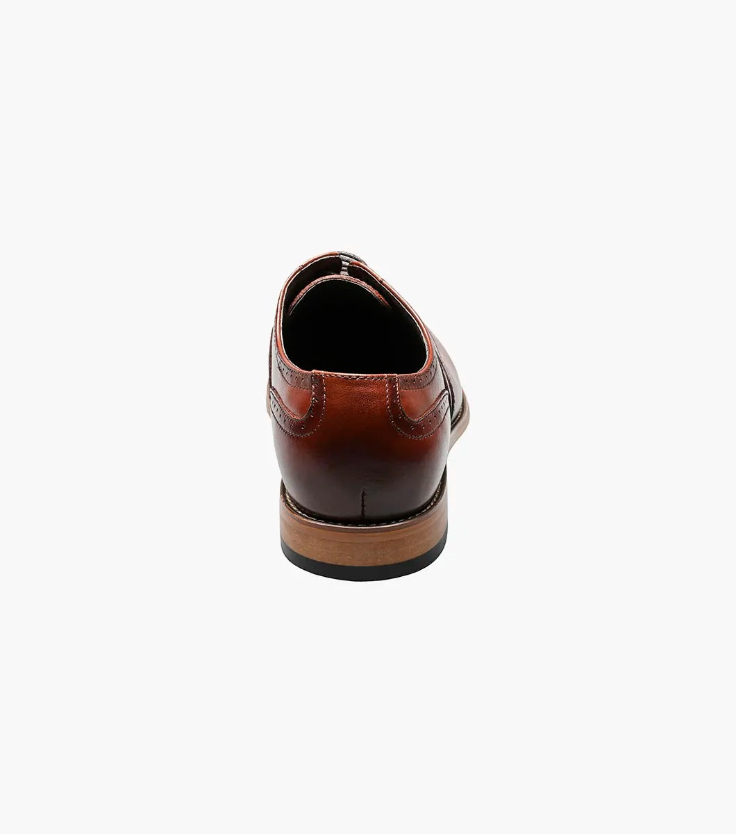 The Stacy Adams DUNBAR Wingtip Oxford shoe, model number 25064-221 in Cognac, showcases a leather upper with intricate stitching and perforations. This elegant design is completed with a low wooden heel, creating timeless sophistication against a white background.