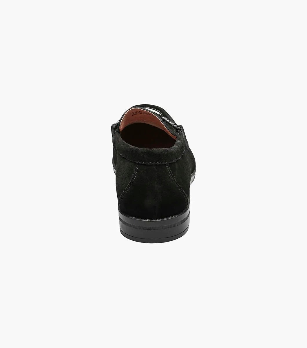 The Stacy Adams NEVILLE Moc Toe Bit Slip On in black suede showcases a metal chain detail on top, accompanied by a slightly elevated heel and stitched accents. Its cushioned insole provides comfort for all-day wear.