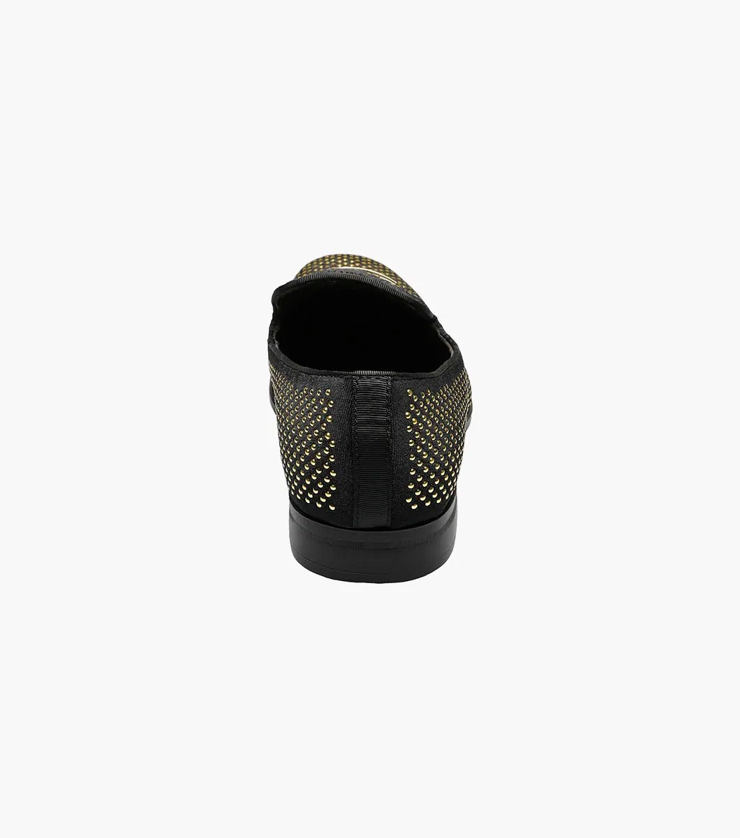 The Stacy Adams - SWAGGER Studded Slip On - Black and Gold - 25228-715 is a black loafer adorned with gold studs and a decorative emblem on top, featuring a comfortable memory foam insole.