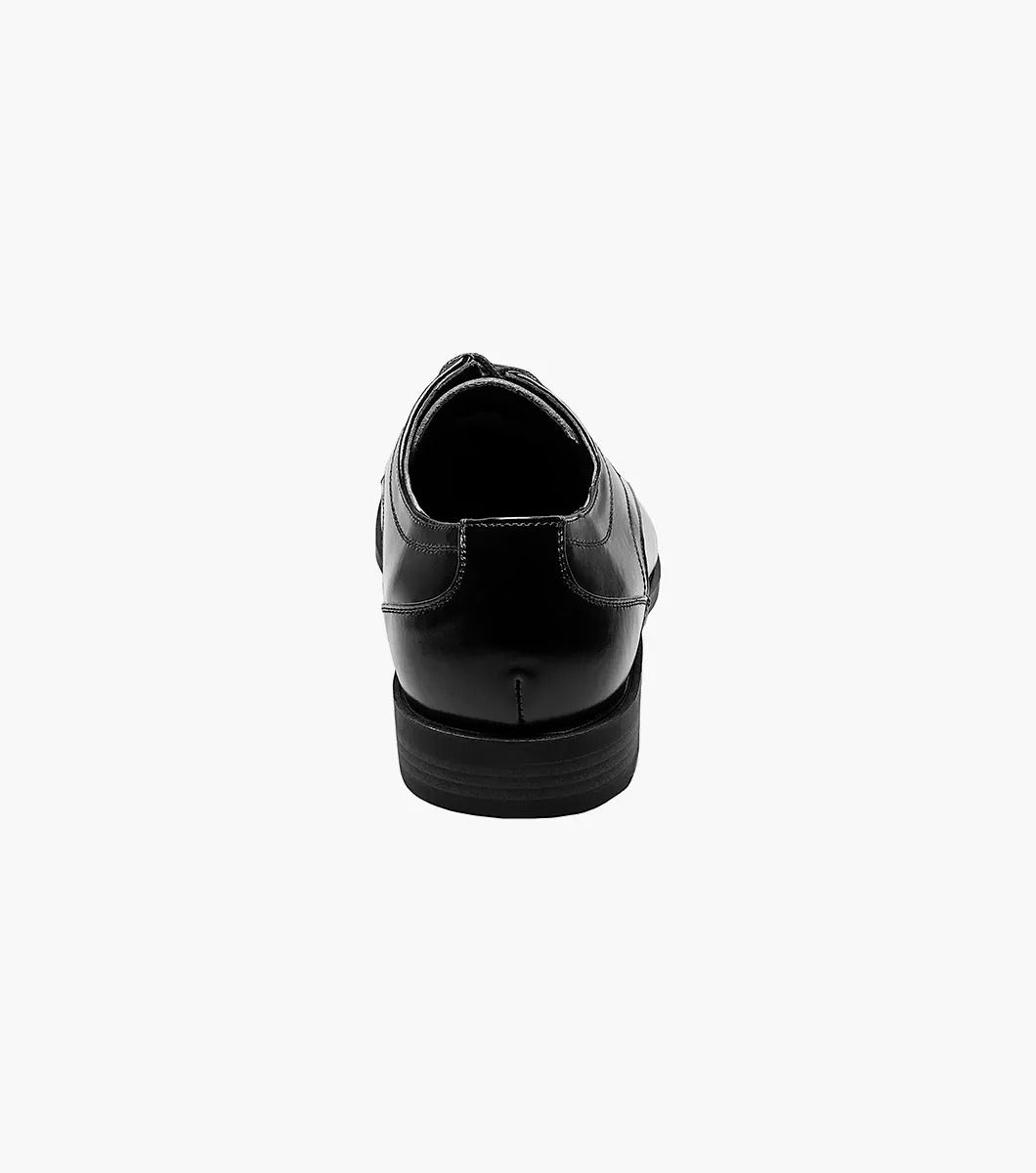 The Stacy Adams Calhoun Moc Toe Oxford, Model 20117-001, is a genuine leather dress shoe in polished black. This STACY ADAMS shoe features laces, a low heel, and boasts a sleek design. It is elegantly displayed against a white background.