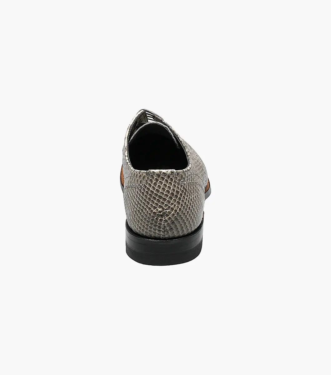 The Stacy Adams Madison Anaconda Plain Toe Oxford in gray showcases a sleek snakeskin pattern, complemented by a black leather outsole and matching laces, all elegantly displayed on a white background.