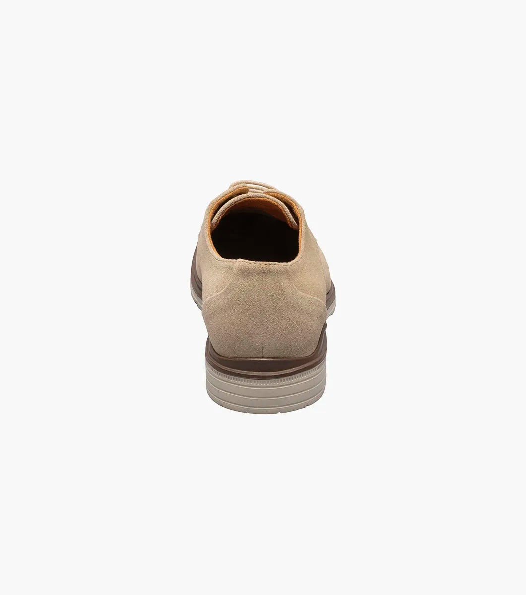 The Stacy Adams TAYSON Plain Toe Lace Up in sandstone is an Oxford shoe made from tan suede. It features anatomical arch support and laces, complemented by a light brown sole. The shoe is displayed against a plain white background.