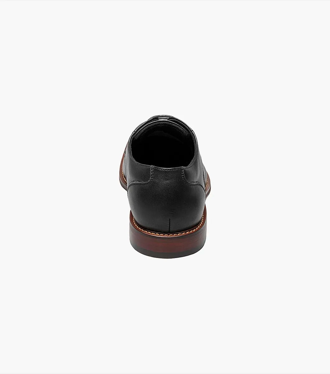 A single Stacy Adams - MARLTON Plain Toe Oxford in black leather, featuring laces, a burnished finish, brown sole, slight heel, and anatomical arch support is displayed on a plain white background.