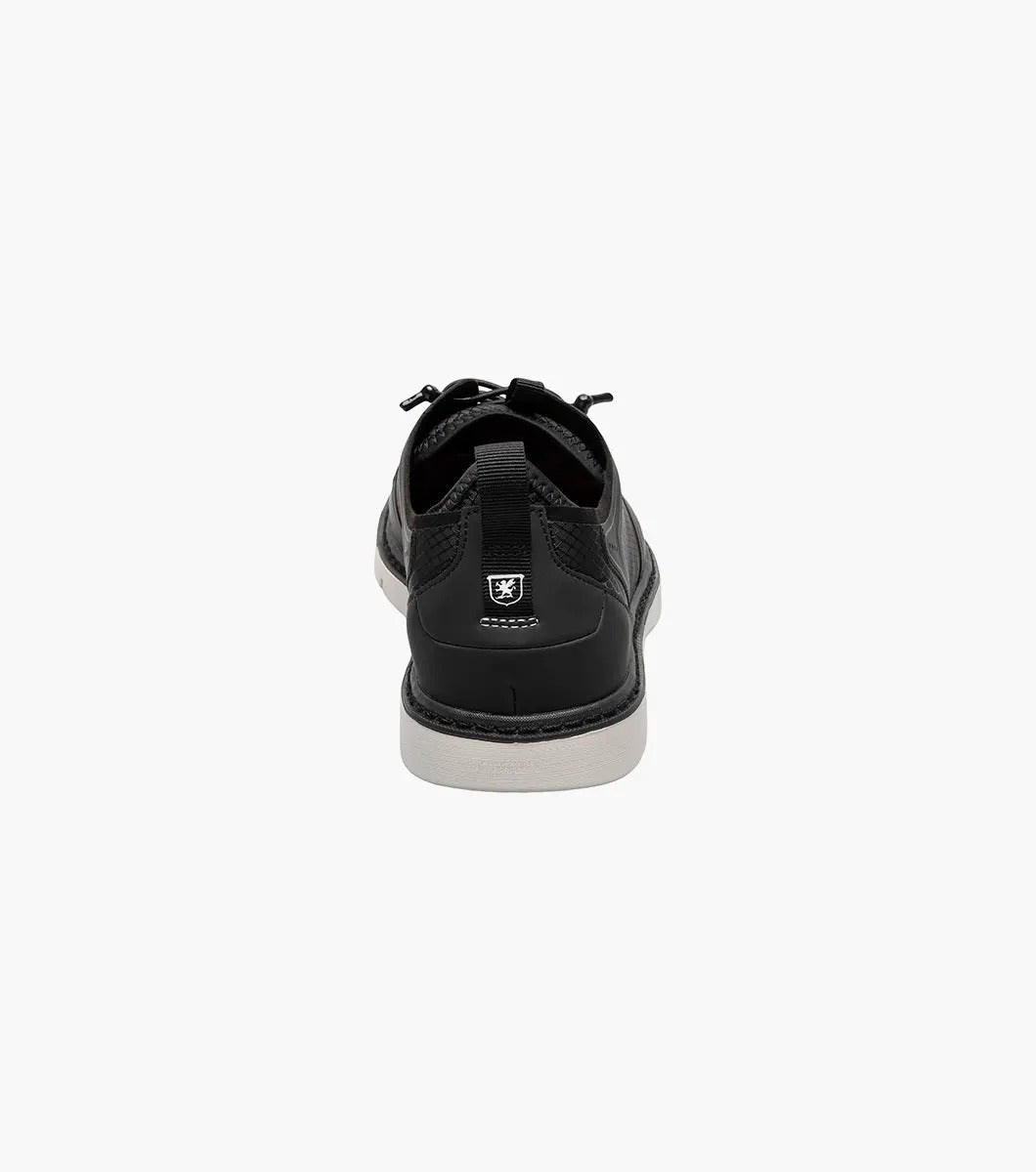 The Stacy Adams SYNCHRO Plain Toe Elastic Lace Up shoe in black (style 25518-001) is a casual dress shoe featuring an elastic lace-up design with a perforated pattern and white sole, complemented by the comfortable RedZone footbed. It is showcased from the side against a simple backdrop.