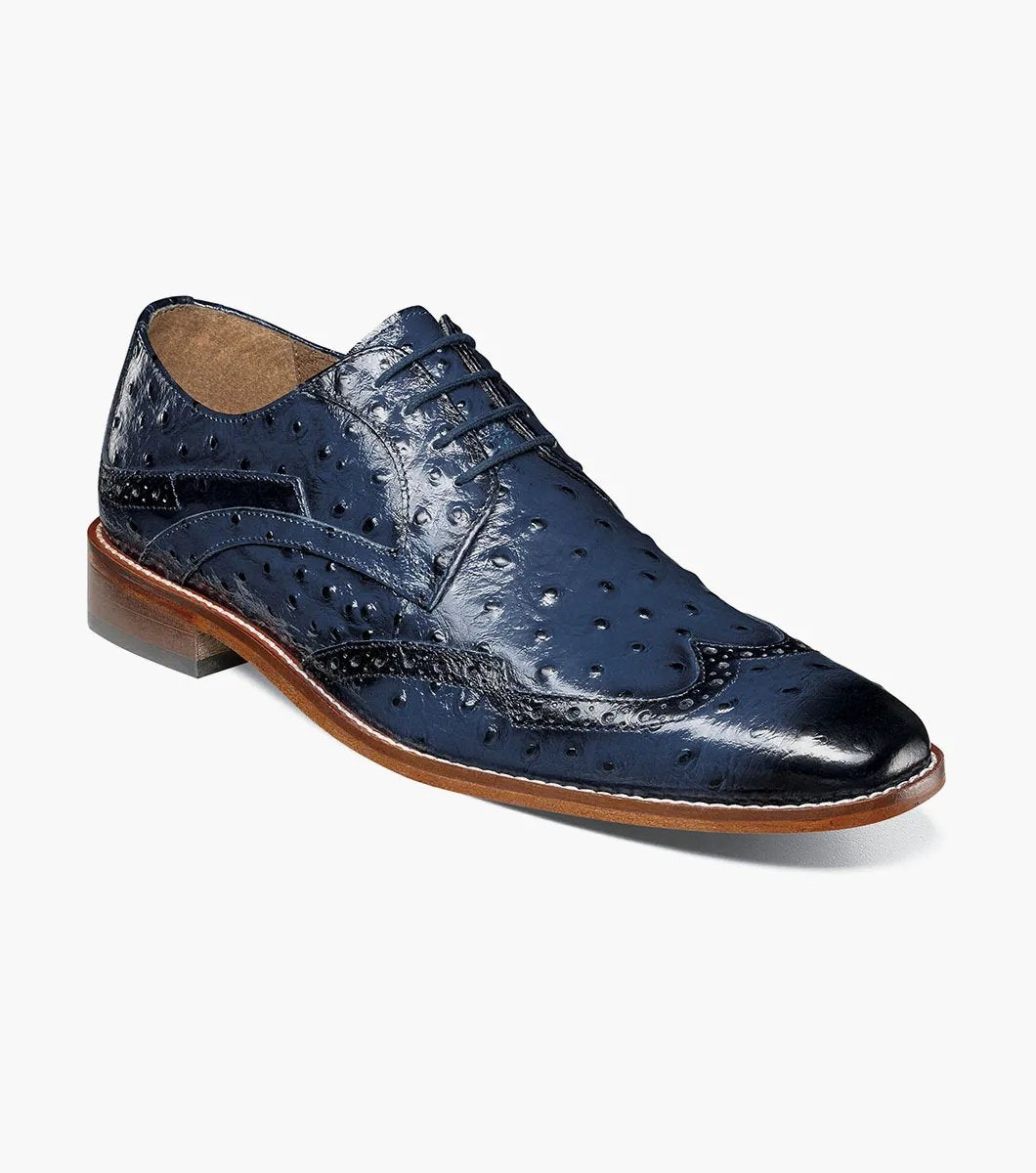 The Stacy Adams GENNARO Wingtip Oxford in blue, style number 25537-400, showcases intricate brogue detailing and comes with a contrasting brown sole. Set against a plain white background, it delivers unparalleled comfort through its anatomical arch support while melding elegance with functionality.