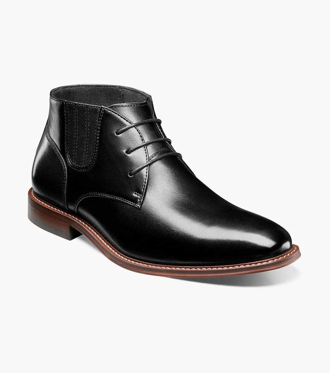 Introducing the Stacy Adams - MAXWELL Plain Toe Chukka Boot in Black, model 25551-001. This versatile boot features a sleek polished finish, a contrasting brown welt, and three pairs of lace eyelets. Set atop a wooden sole, it is designed with anatomical arch support to ensure maximum comfort.