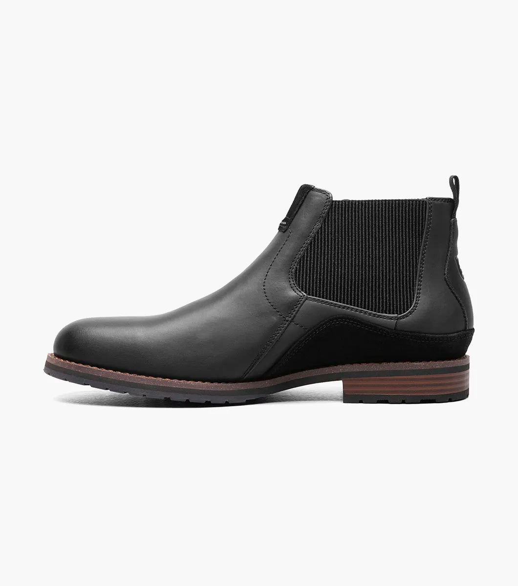 The Stacy Adams OSKAR Plain Toe Chelsea Boot in Black Waxy features a black leather design with a side buckle, an elastic gusset, and a brown sole. Its stylish mixed material upper adds an extra touch of flair.