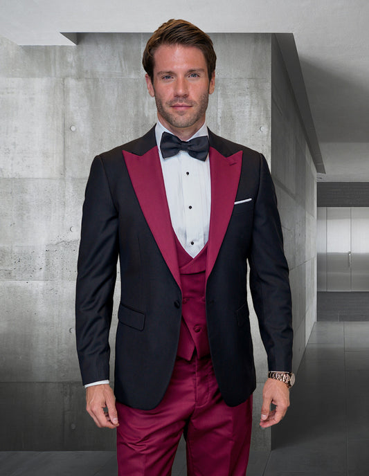 A man in a STATEMENT CLOTHING | ARYA-BURGUNDY tuxedo suit from Statement Clothing, exuding a sleek and modern fit crafted from luxurious Italian fabric, stands in a contemporary, concrete room.