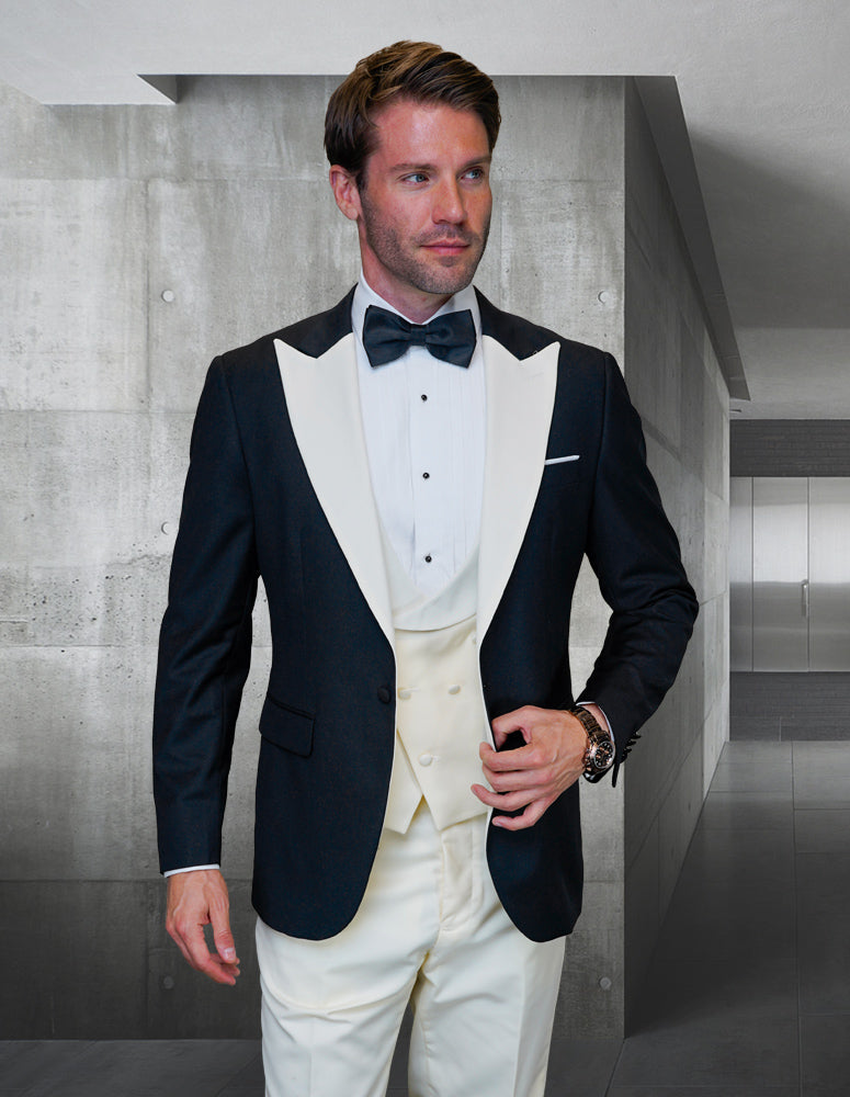 A man wearing the sophisticated black ARYA-IVORY tuxedo suit by Statement Clothing, crafted from exquisite Italian fabric, paired with a white shirt and bow tie, stands in a modern, minimalist hallway.