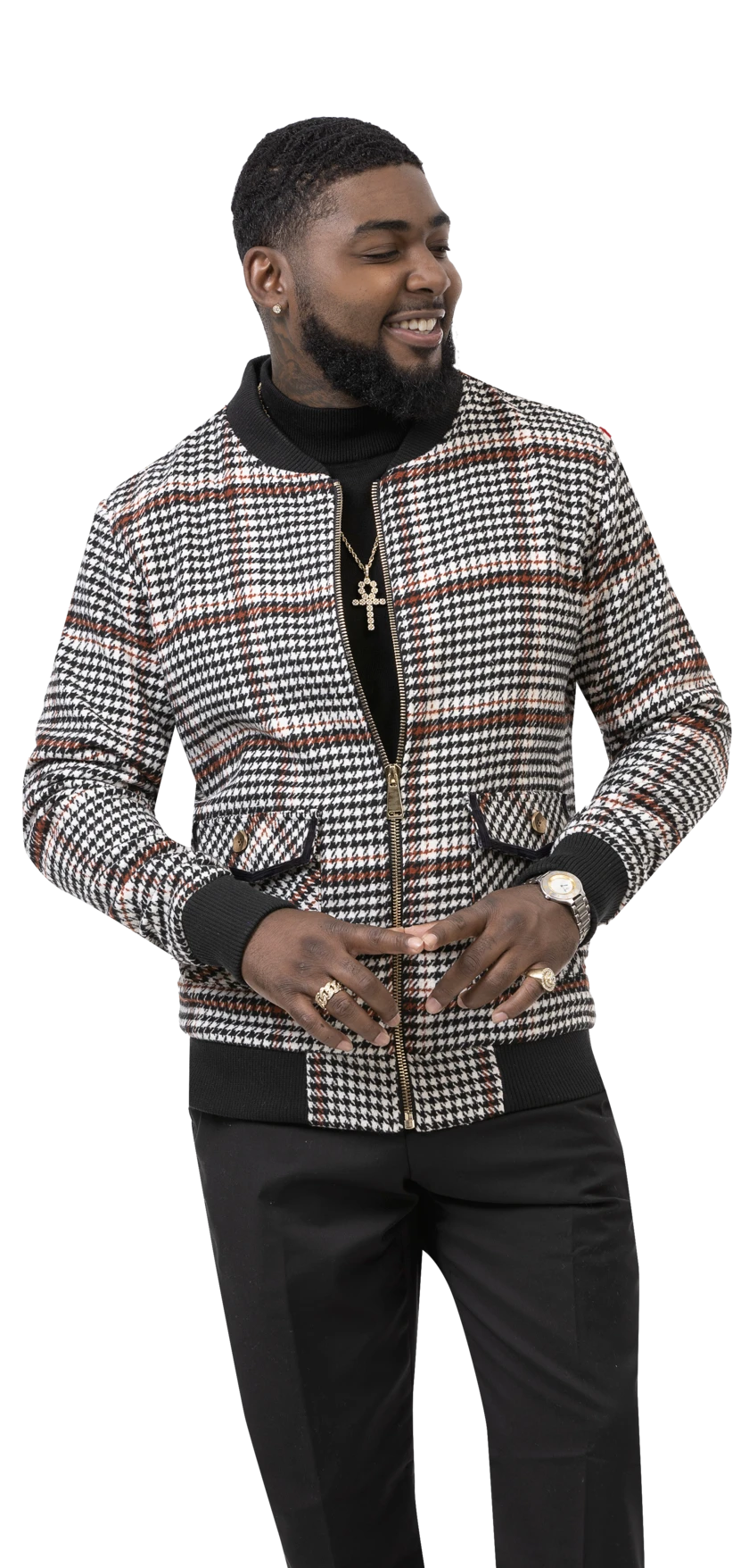 A man confidently smiles while wearing the EJ Samuel Houndstooth Bomber Jacket B102, stylishly clutching the collar. His outfit is completed with a turtleneck, black pants, and an assortment of jewelry including rings, a watch, and a cross necklace. The timeless pattern of his EJ SAMUEL jacket stands out as impressively as any contemporary plaid design.