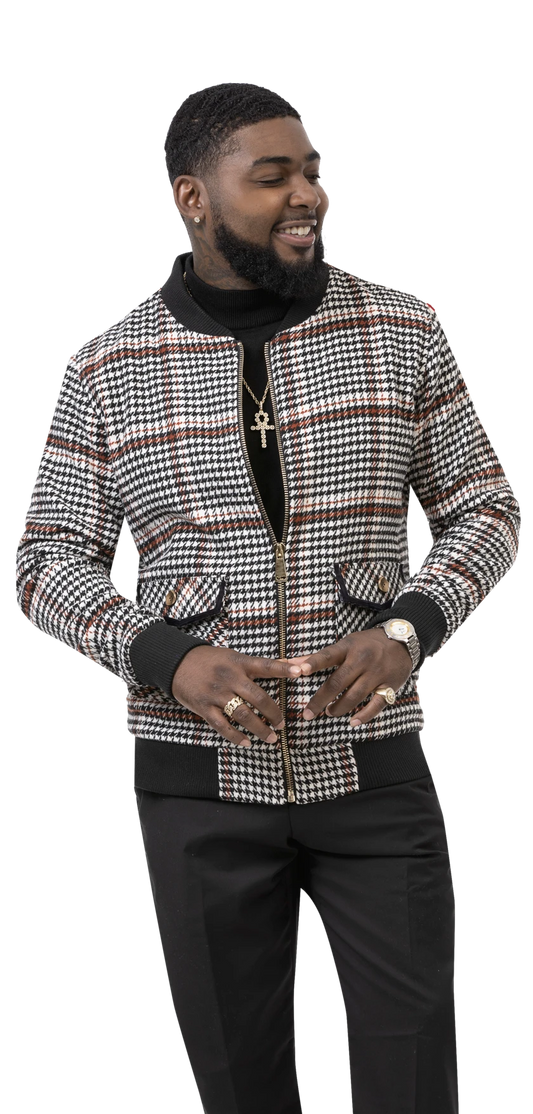 A man confidently smiles while wearing the EJ Samuel Houndstooth Bomber Jacket B102, stylishly clutching the collar. His outfit is completed with a turtleneck, black pants, and an assortment of jewelry including rings, a watch, and a cross necklace. The timeless pattern of his EJ SAMUEL jacket stands out as impressively as any contemporary plaid design.