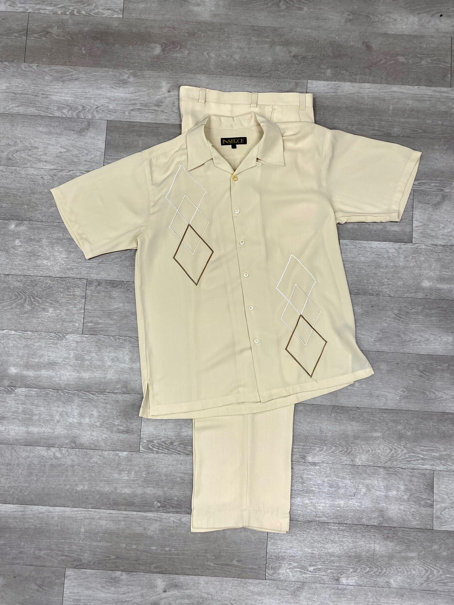 The Inserch 2pc 9356 Beige set, crafted from soft microfiber with geometric designs, features a beige short-sleeve shirt and pant ensemble elegantly displayed on a wooden floor. This model introduces a modern touch of elegance to any wardrobe.