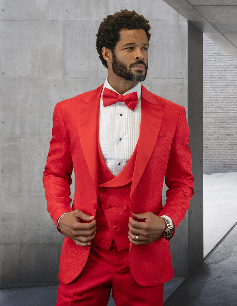 A gentleman dressed in a Statement Clothing | BELAGIO15-RED suit featuring a tailored fit with flat front pants and accessorized with a bow tie is positioned by a concrete wall and archway.