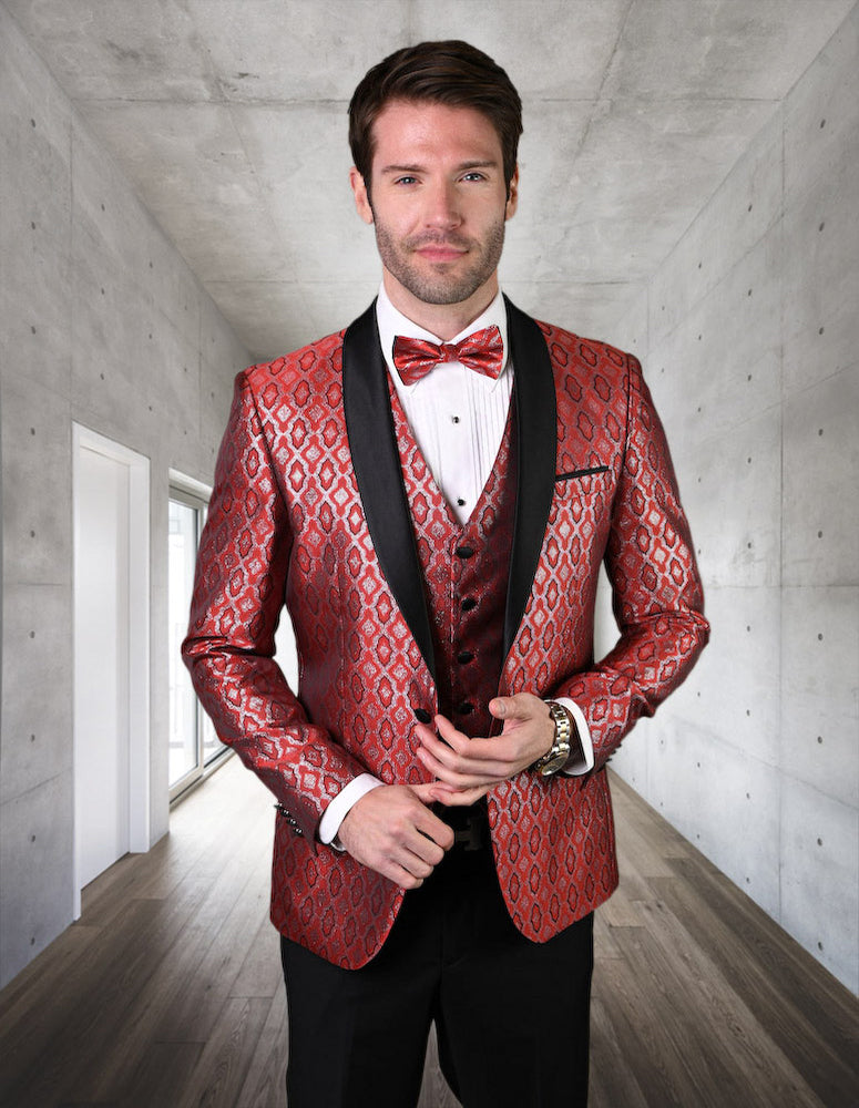 A man dressed in Statement Clothing's BELAGIO21-RED suit, featuring a red patterned design with slim fit flat front pants, complemented by a bow tie, stands in a modern, gray room with wooden flooring.