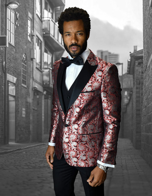 A man wearing the BELLAGIO-4-RED ensemble from Statement Clothing, featuring a textured red and black suit with slim-fit pants and a bow tie, stands confidently in an urban alleyway.