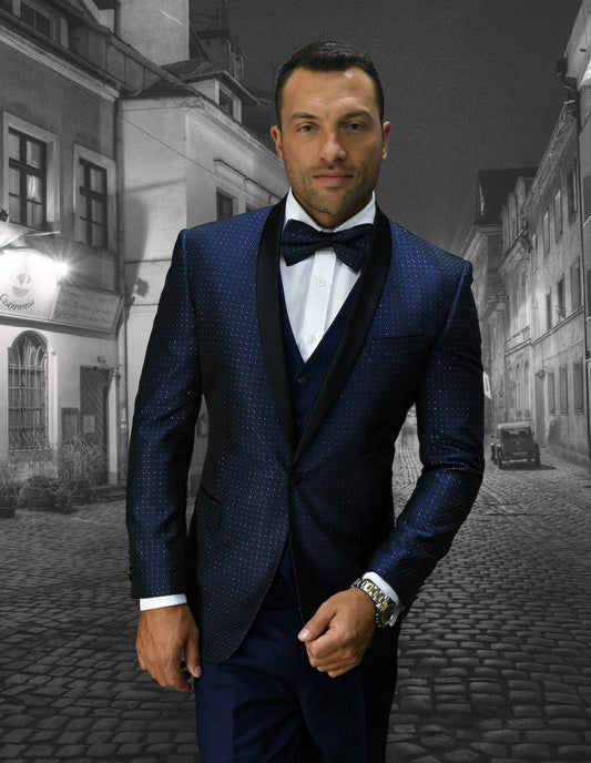 A man in a Statement Clothing Bellagio-6-Navy dark, textured suit featuring slim-fit navy pants and a bow tie stands confidently on a cobblestone street, framed by old buildings.