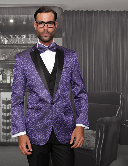 A person wearing glasses and the Bellagio-Purple slim fit tuxedo by Statement Clothing, featuring flat front pants and a purple pattern, stands in a room with a dark curtain and a shelf filled with glassware in the background.