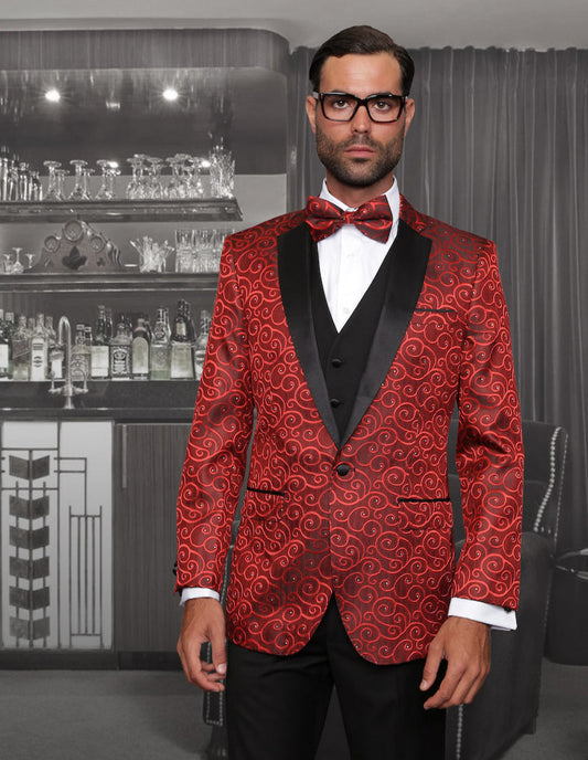 A man wearing the Statement Clothing | Bellagio-Red tuxedo, featuring a red patterned design with slim fit flat front pants, a black lapel, and a bow tie, stands in front of a home bar adorned with shelves of glassware and bottles.