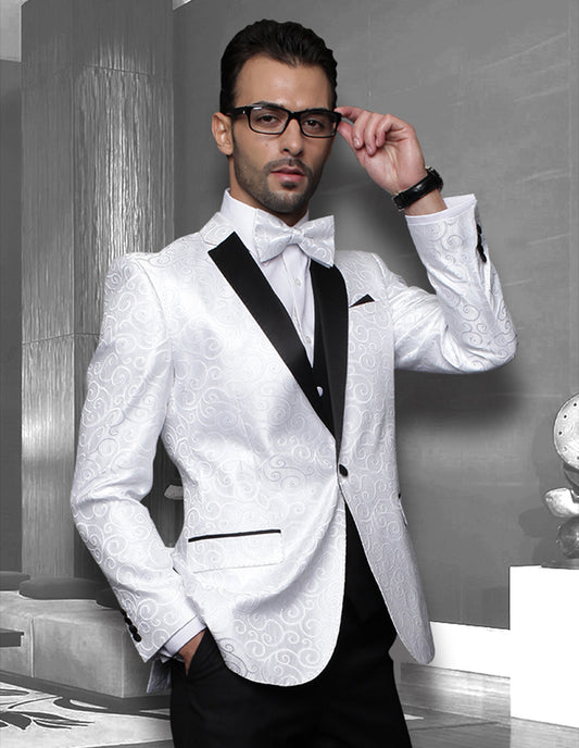 A man in the Bellagio-White tuxedo by Statement Clothing, featuring a slim fit and white pattern with black lapels, embodies sophistication as he adjusts his glasses. He stands confidently in a modern interior setting, exuding elegance and style.