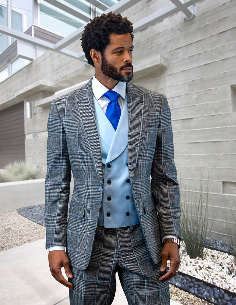 A man in a STATEMENT CLOTHING | BENSON-POWDER suit, featuring a tailored fit crafted from fine Italian wool, paired with a blue tie and vest, stands in front of a modern concrete building.