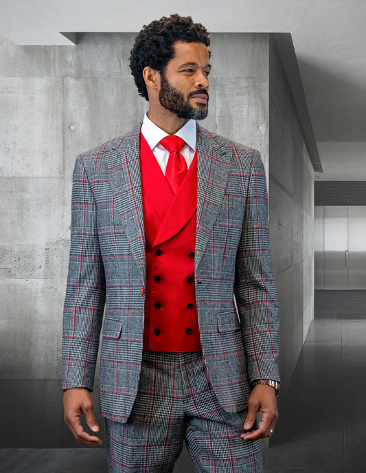 A man wearing the STATEMENT CLOTHING | BENSON-RED ensemble, featuring a tailored-fit gray checkered suit made from Italian wool and paired with a red vest and tie, stands in a modern concrete hallway.